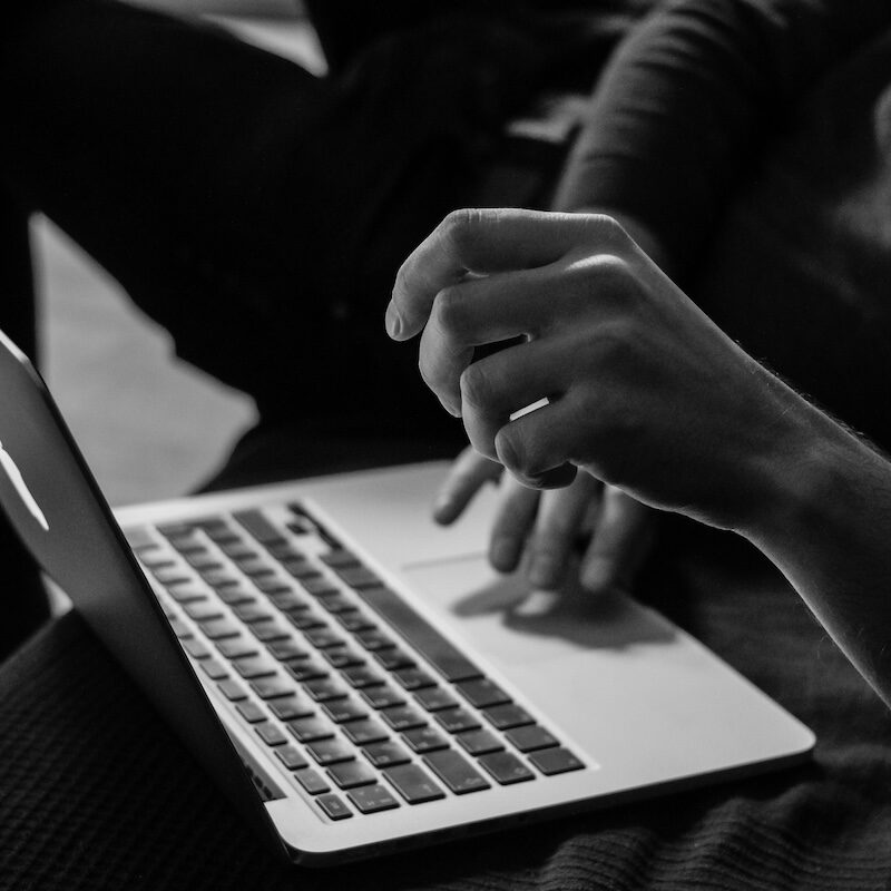 a black and white image shows a laptop open with a hand on the trackpad.