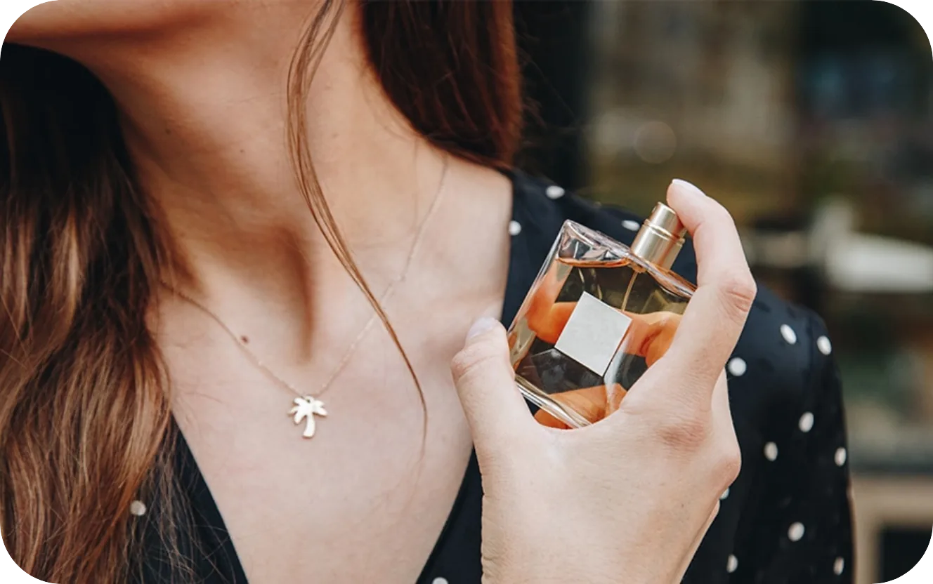 Woman wearing a palm tree necklace applies perfume from a glass bottle near her neck. Woman wearing a palm tree necklace applies perfume from a glass bottle near her neck.