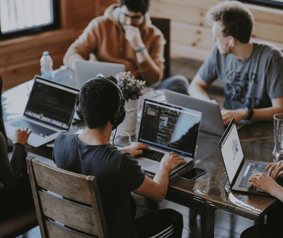 People working on laptops around a wooden table in a collaborative office workspace.