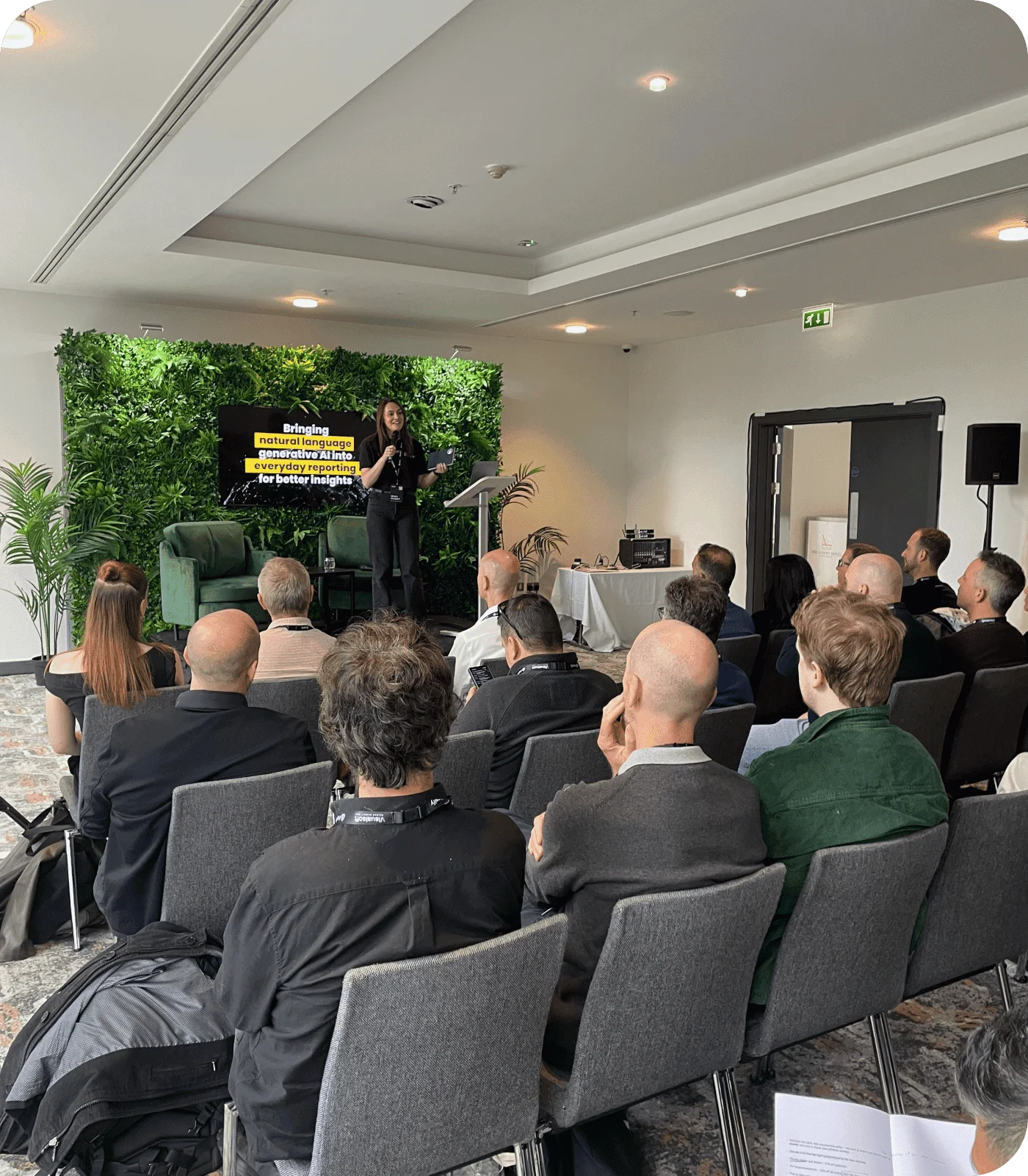 Speaker presenting on generative AI for reporting at one of our events and webinars, with an audience seated in a conference room.