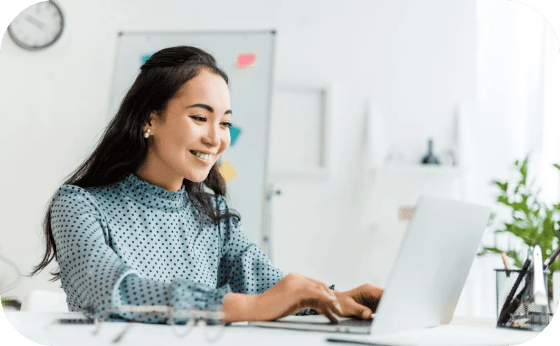 Smiling woman using a laptop to review AI Reporting data in a bright office setting.