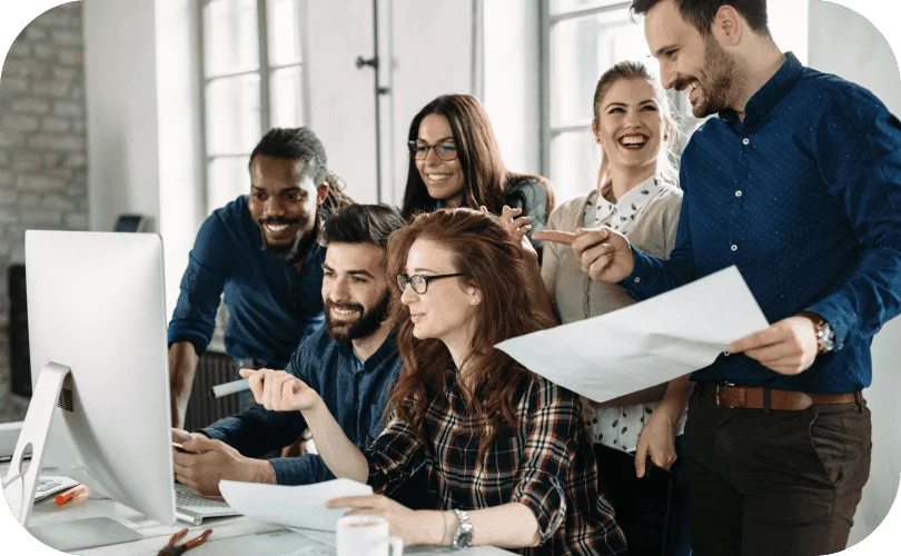 Team of six colleagues smiling and reviewing data on a computer screen while discussing AI reporting insights.