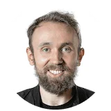 Man with short gray hair and a dark beard smiling, wearing a black top against a white background.