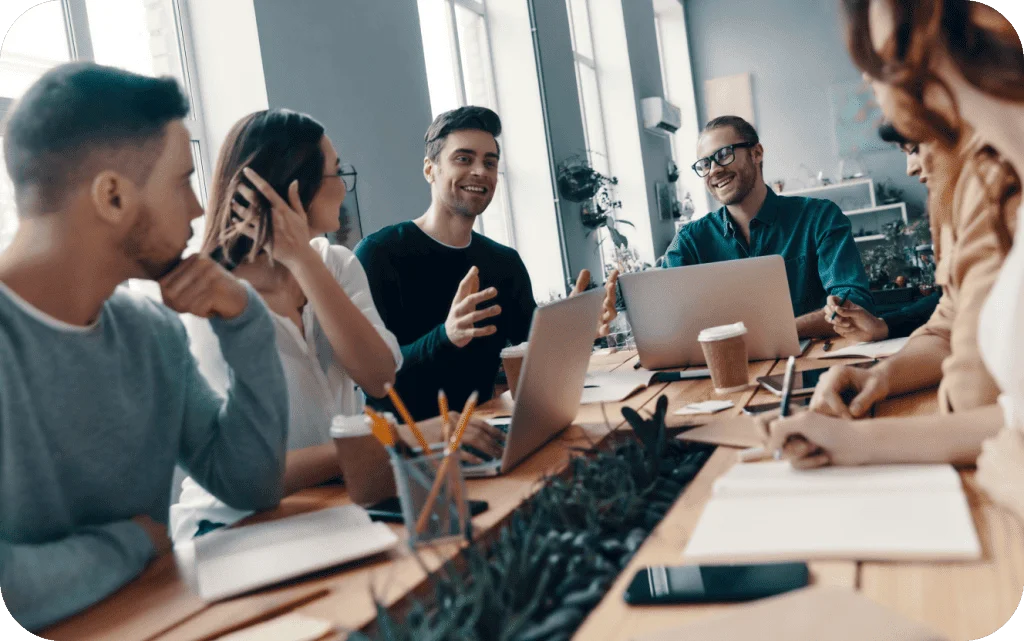 Team of colleagues having an engaging discussion around a table with laptops during a business meeting.