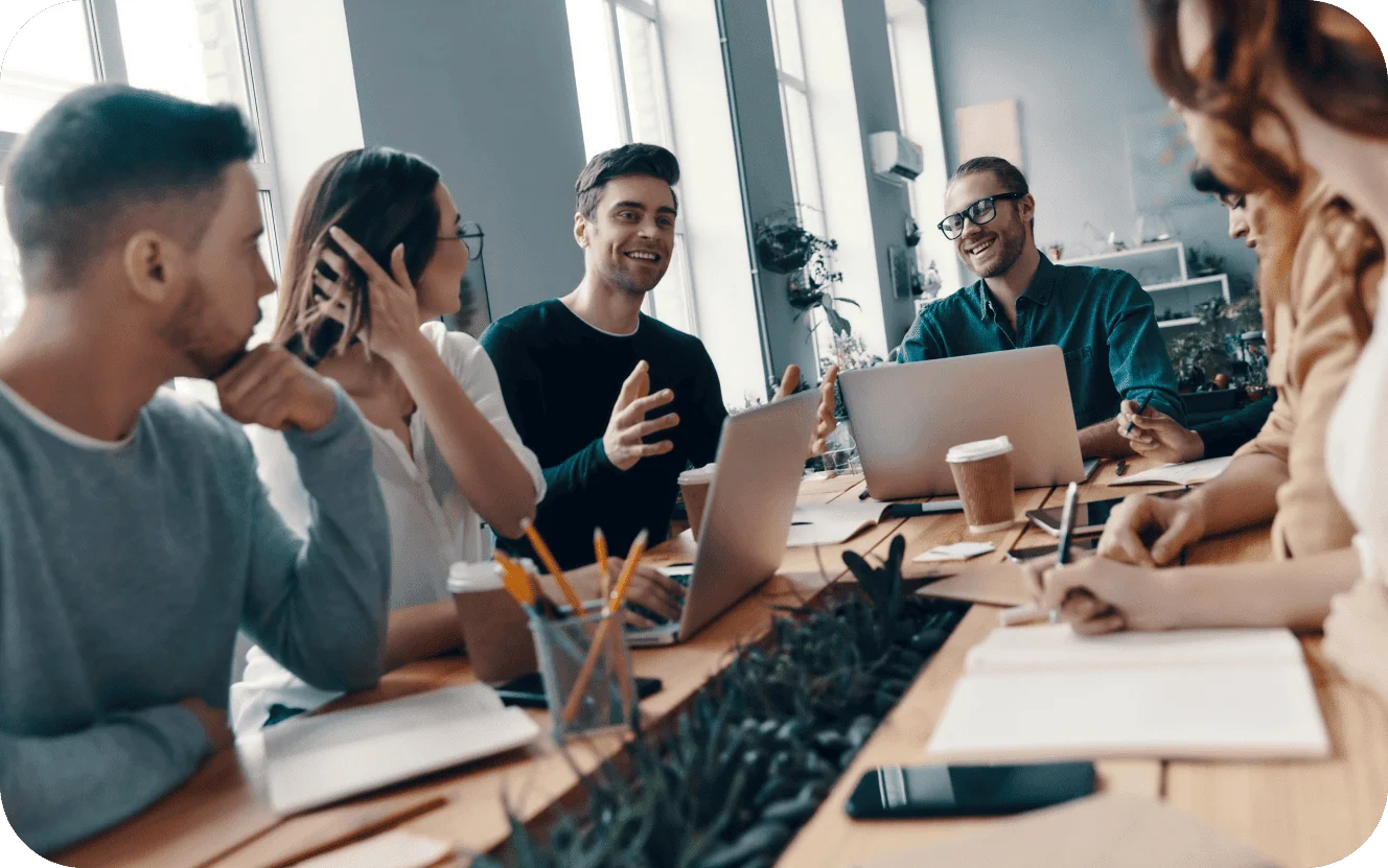 Team of colleagues having an engaging discussion around a table with laptops during a business meeting.