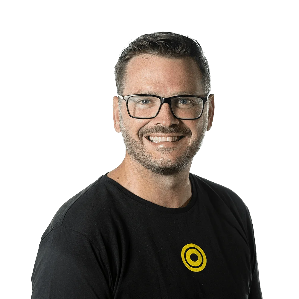 Smiling man with glasses and a mustache wearing a black t-shirt with a yellow circular logo.