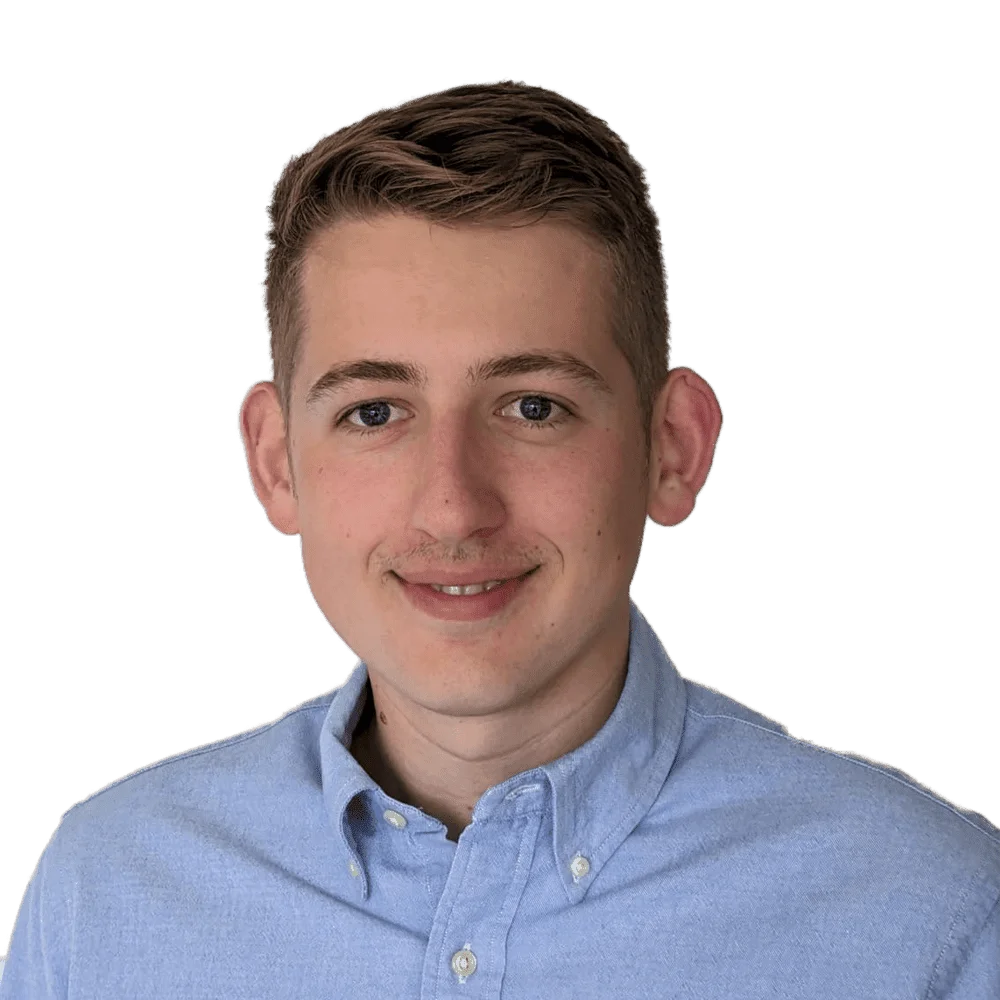 Young man with short brown hair smiling in a light blue button-down shirt, professional headshot.