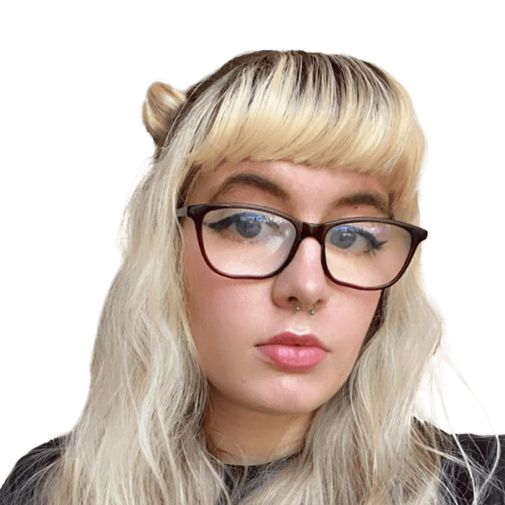 Close-up selfie of a young woman with blonde hair, bangs, glasses, and a septum piercing.