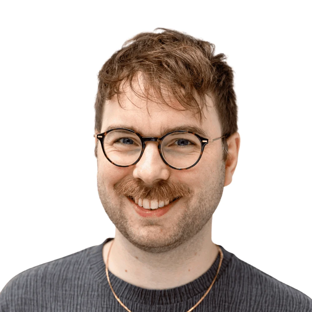 Headshot of a smiling young man with round glasses, a mustache and beard, wearing a gray sweater.