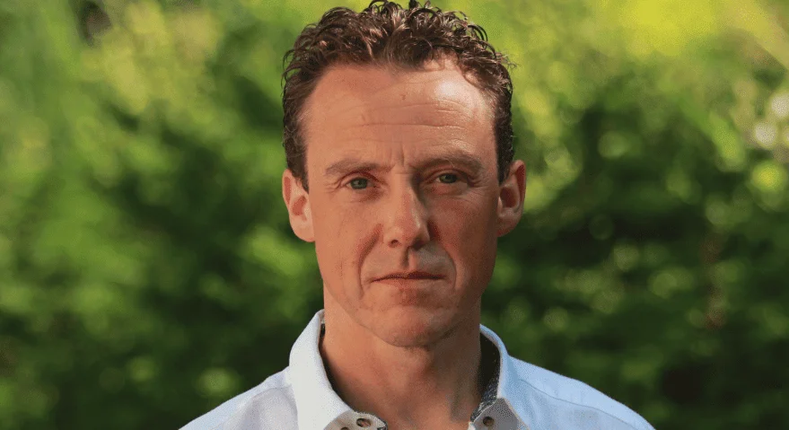 Man with curly hair and a white shirt standing outdoors, representing the about ask bosco team page.